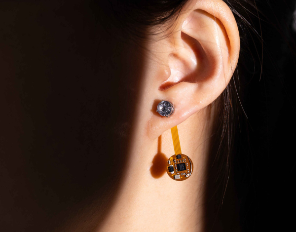 Electronics attached to an earring, worn by a person covered by shadow